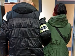 Policjant doprowadza zatrzymaną kobietę do jednostki penitencjarnej