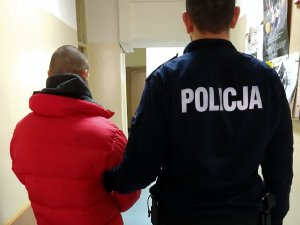 Policjant podczas doprowadzenia zatrzymanego mężczyzny do komisariatu Policji