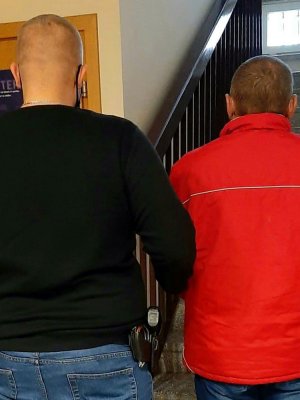 Nieumundurowany policjant doprowadza zatrzymanego mężczyznę na czynności procesowe do prokuratury