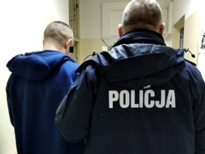 Umundurowany policjant doprowadza zatrzymanego mężczyznę do komisariatu na czynności procesowe
