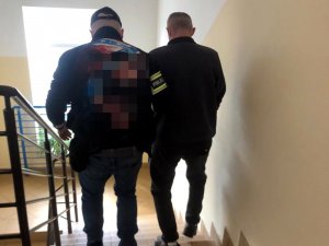 Nieumundurowany policjant doprowadza zatrzymanego mężczyznę do komendy