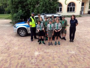 Policjanci wspólnie z harcerzami na tle oznakowanego radiowozu