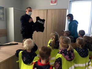 Dzielnicowy prezentuje dzieciom policyjny sprzęt wykorzystywany w służbie