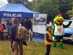 Wuzetek, maskotka Powiatu Warszawskiego Zachodniego na tle oznakowanego radiowozu