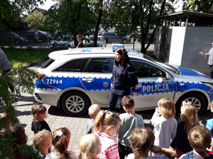 Umundurowana policjantka prezentuje dzieciom radiowóz
