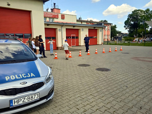 Policjanci na placu na tle oznakowanego radiowozu podczas spotkania z dziećmi