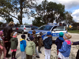 Policjant przy radiowozie prezentuje pojazd przedszkolakom