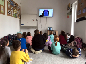 Dzieci w sali edukacyjnej podczas spotkania z policjantami oglądają film edukacyjny