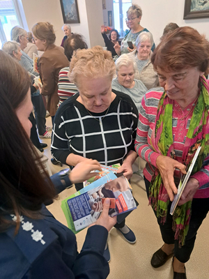 Policjantka rozdaje seniorom ulotki informacyjne