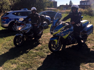 Policjanci ruchu drogowego na motocyklach, w tle oznakowany radiowóz