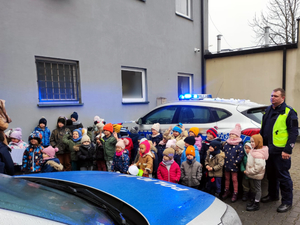 Umundurowany policjant z dziećmi na tle oznakowanego radiowozu