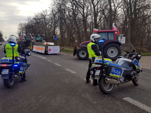 Umundurowani policyjni motocykliści zabezpieczają wjazd  kolumny maszyn rolniczych na drogę krajową 92