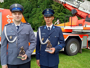 Umundurowani policjanci z wyróżnieniem na tle pojazdu Straży Pożarnej