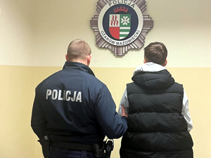 Umundurowany policjant doprowadza zatrzymanego mężczyznę do komisariatu na czynności procesowe