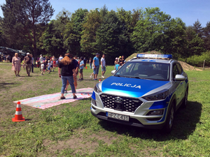 Uczestnicy pikniku przy stoisku policyjnym obok oznakowanego radiowozu