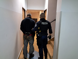 Policjant doprowadza zatrzymanego mężczyznę do komendy