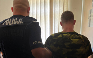 Umundurowany policjant prowadzi zatrzymanego mężczyznę