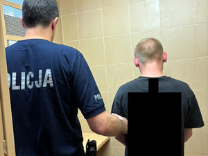 Umundurowany policjant prowadzi zatrzymanego mężczyznę