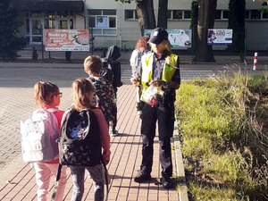 Policjantka przed szkołą rozdaje uczniom elementy odblaskowe