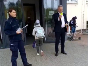 Policjantka z Burmistrzem Łomianek rozdaje odblaski dzieciom przed szkołą