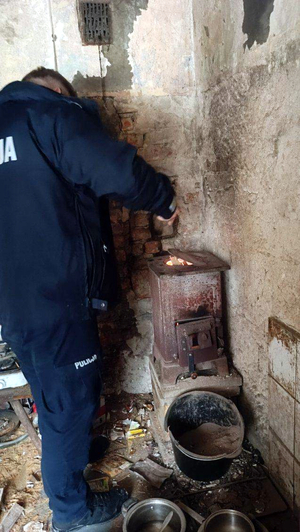 Dzielnicowy pomaga mieszkańcowi napalić w piecu